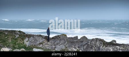 Un'immagine panoramica di una persona in piedi su Towan Head che guarda il tempo selvaggio causato da Storm Eunice quando arriva sulla costa nord della Cornovaglia in Foto Stock