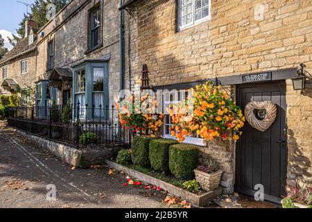 Begonias fiorito in cesti pendenti fuori Clematis Cottage nella città Cotswold di Burford, Oxfordshire, Inghilterra Regno Unito Foto Stock