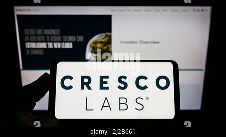 Persona che tiene smartphone con logo della società americana di cannabis Cresco Labs Inc. Sullo schermo di fronte al sito web. Mettere a fuoco sul display del telefono. Foto Stock