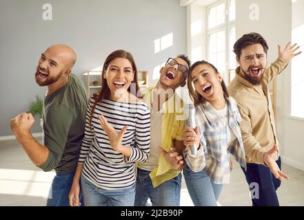 Compagnia di amici che cantano insieme le loro canzoni preferite sul microfono karaoke durante la festa di casa. Foto Stock