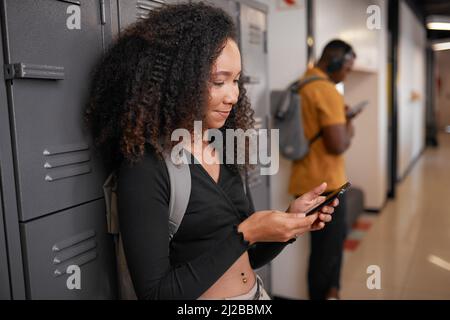 Una giovane studentessa femminile con un maschio sui loro telefoni in un corridoio di armadietto dell'università Foto Stock