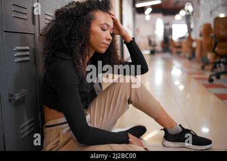 Un giovane studente si siede da solo nel corridoio della scuola che ha un aspetto infelice e depresso Foto Stock