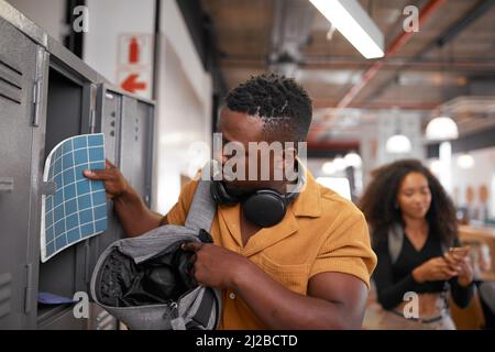 Una giovane studentessa nera porta la sua borsa mentre una donna cammina sul suo telefono Foto Stock