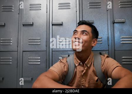 Un giovane studente del Sud Est asiatico siede di fronte agli armadietti del campus sorridendo Foto Stock