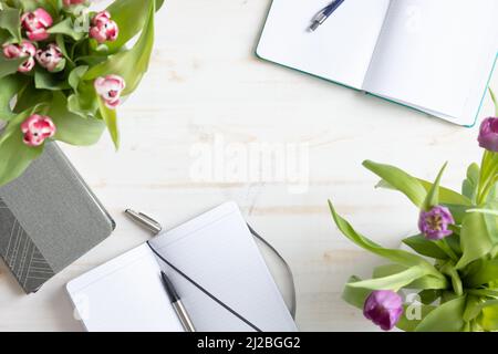 Due taccuini vuoti aperti e due mazzi di tulipani su un tavolo di legno bianco con spazio di copia girato dall'alto Foto Stock