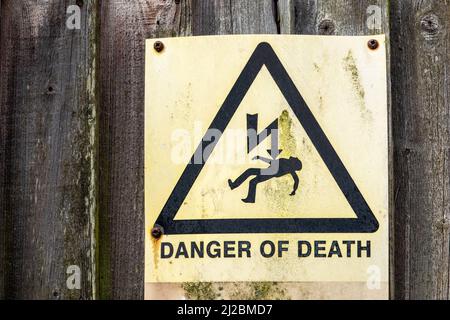 Pericolo di morte cartello di avvertimento molto sbiadito e macchiato montato su una sezione di recinzione di legno fortemente stagionata Foto Stock