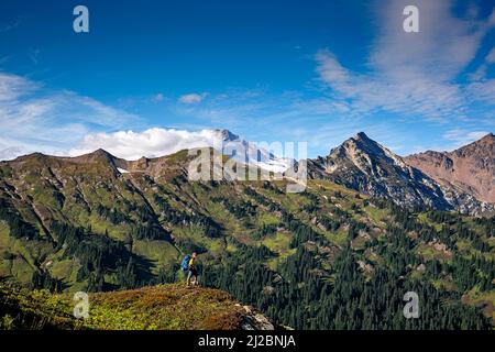 WA21213-00...WASHINGTON - Hiker in collina che domina la White River Valley dal Pacific Crest Trail con Glacier Peak in lontananza; Glacier Pea Foto Stock