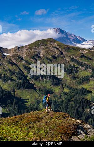 WA21214-00...WASHINGTON - Hiker in collina che domina la White River Valley dal Pacific Crest Trail con Glacier Peak in lontananza; Glacier Pea Foto Stock