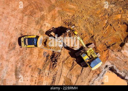 Il luogo di preparazione per la costruzione di case residenziali sulla benna del trattore sta riempiendo un terreno nel camion Foto Stock