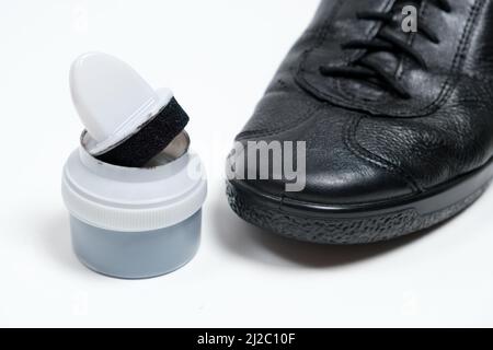 Crema per calzature con spugna e scarpe nere in pelle da uomo su sfondo bianco. Cura delle scarpe Foto Stock
