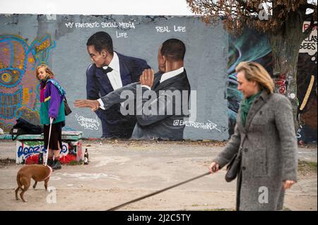 30.03.2022, Berlino, Germania, Europa - due donne camminano i loro cani davanti a un graffito dell'artista EME Freethinker su un segmento del muro di Berlino. Foto Stock