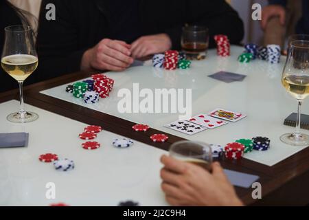 Uomo e donna in un gioco di poker. Patatine, carte, bicchieri di whiskey e champagne sul tavolo con riflessione. Fotografia di stile di vita. Notte di poker. Foto Stock