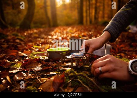 La donna usa un riscaldatore a gas portatile e una padella per cucinare all'aperto Foto Stock