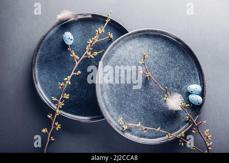 Decorazioni di Pasqua. Piatto fatto a mano decorato con uova blu, piume e rametti primaverili. Piastra in ceramica su sfondo grigio. Foto Stock