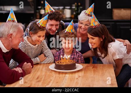 Faccia un desiderio prima che li soffiate fuori. Scatto di un ragazzo felice che festeggia il suo compleanno con la sua famiglia. Foto Stock