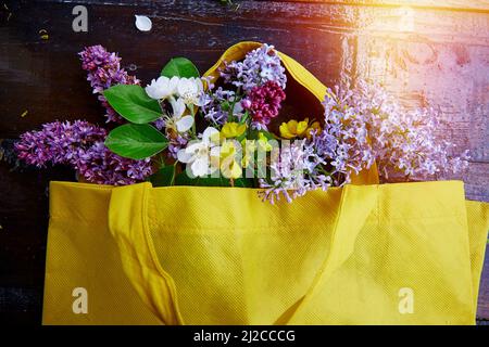 Bouquet primaverile di gigli, fiori di albicocca, fiori in un sacchetto giallo. Sostenibile, cottage core, connessione con il concetto di natura. Foto Stock