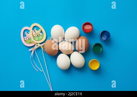 Modello a tema pasquale con uova di pollo e pitture su sfondo blu Foto Stock