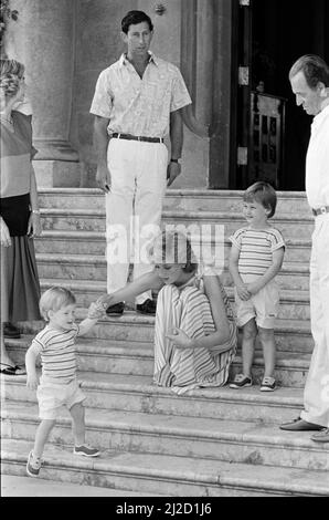 S.A.R. la Principessa Diana, la Principessa del Galles e suo marito S.A.R. il Principe Carlo, il Principe di Waleson in vacanza a Palma di Maiorca. Sono gli ospiti del re Juan Carlos (a destra - quasi fuori dal colpo) e di sua moglie Sofia (a sinistra), e sono raffigurati qui al Marivent Palace, Palma, Maiorca. In questa foto la principessa Diana aiuta il suo figlio di quasi 2 anni, il principe Harry manager i passi. Il fratello maggiore Prince William guarda avanti. Foto scattata il 9th agosto 1986 Foto Stock