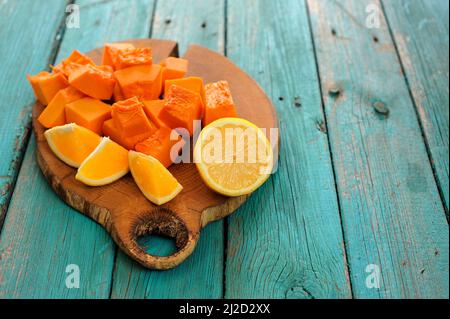 Zucca dolce butternut, arancio e limone tagliato su tavola di legno su tavola turchese copyspace Foto Stock