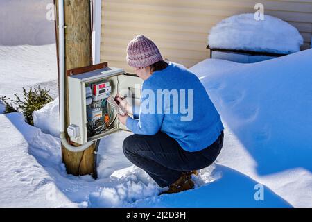 La donna sta prendendo le letture dal contatore elettrico esterno all'aperto in campagna nella giornata di inverno. Foto Stock