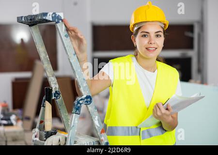 Ingegnere civile positivo femmina che prende appunti durante il controllo del cantiere Foto Stock