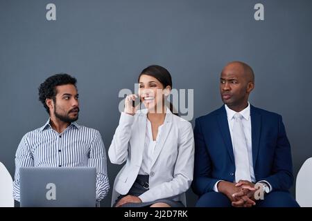 Questa chiamata potrebbe rivelare chi ha ottenuto il lavoro. Studio di imprenditori aziendali in attesa in linea su sfondo grigio. Foto Stock