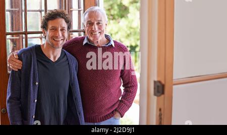 La mela non cade lontano dall'albero. Un ritratto corto di un padre felice e di suo figlio adulto in piedi a casa. Foto Stock