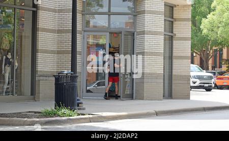 Gen Z uomo in pantaloncini rossi e maglietta nera che entra in un negozio a Southlake Town Square; Southlake, Texas Foto Stock