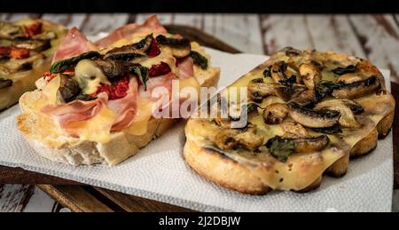 Bruschette grandi con formaggio, funghi, prosciutto e pomodoro in diverse combinazioni. Concetto di cucina mediterranea. Foto Stock