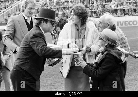 La pop star e Watford FC Presidente, Elton John, distribuendo le uova di Pasqua per i fan. Watford V Southampton partita di calcio. Il 6 aprile 1985. Foto Stock