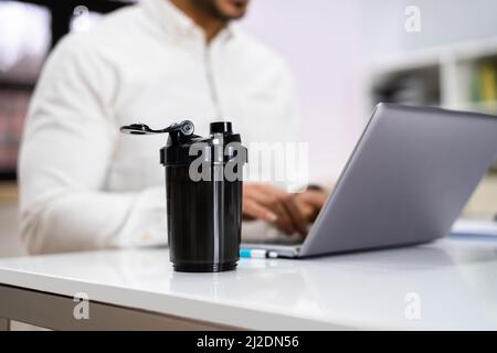 Protein Shake su scrivania e uomo in primo piano utilizzando il computer Foto Stock