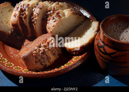 Fette di pane dolce con pezzi di noci sulla parte superiore, su un piatto messicano di fango o argilla e una tazza calda di caffè o cioccolato sul lato Foto Stock