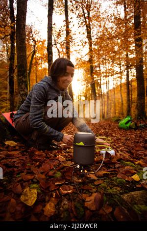 La donna usa un riscaldatore a gas portatile e una padella per cucinare all'aperto Foto Stock