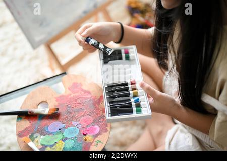 Una ragazza gode colorare i colori acrilici a casa sua, scegliendo un colore per la sua opera d'arte. Concetto di attività creativa per bambini Foto Stock
