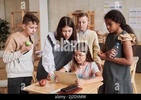 Un gruppo diversificato di bambini che usano un tablet digitale in classe durante la pausa Foto Stock