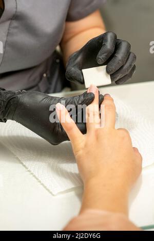 Primo piano delle mani caucasiche di un manicurista professionale stanno archiviando le unghie di una giovane donna. Giovane donna caucasica che riceve una manicure da un estetista con una lima del chiodo in un salone del chiodo Foto Stock