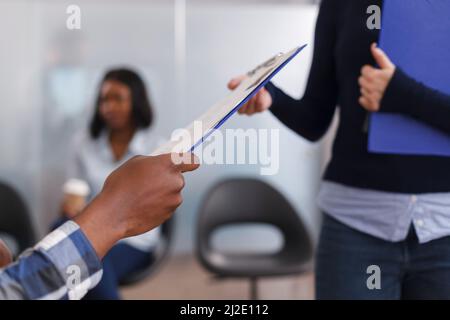 Primo piano delle mani dell'uomo afroamericano che danno il CV del responsabile del reparto di occupazione e la domanda di lavoro mentre nell'area della lobby. Donna d'affari che riceve gli appunti del candidato con i documenti. Foto Stock