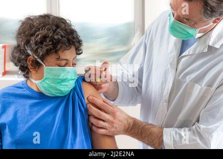 Medico di sesso maschile in maschera protettiva guanti in lattice che danno la vaccinazione intramuscolare protetto braccio del paziente Foto Stock