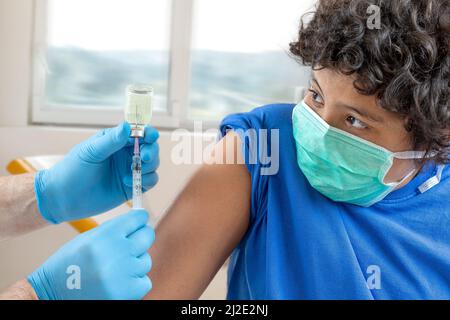 Medico di sesso maschile in maschera protettiva guanti in lattice che danno la vaccinazione intramuscolare protetto braccio del paziente Foto Stock