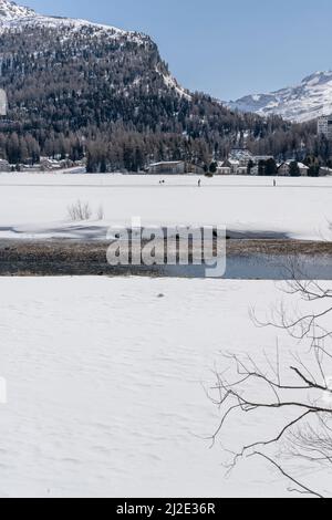 Paesaggio invernale con sciatori di langlauf sulle rive innevate della locanda con la catena montuosa sullo sfondo , girato in luce brillante vicino a Sils, Grigioni, Svizzera Foto Stock