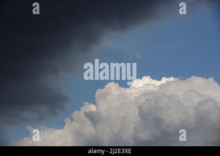 Una nuvola bianca si scontra con una nuvola di tuono scuro contro uno sfondo di cielo blu e luce solare Foto Stock