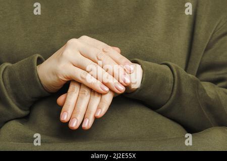 Mani donna con manicure perfetto. Mani di una ragazza in un primo piano verde felpa cappuccio Foto Stock