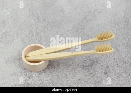 Due spazzolini da denti in legno in un supporto originale su sfondo in cemento. Spazzolini ecologici Foto Stock