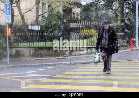 Ginevra, Svizzera, 2022-04-01 l'uomo attraversa la strada attraverso la neve. Il primo giorno di aprile è iniziato con il tempo del vino. Credit: marcio cimatti/Alamy Live News Foto Stock