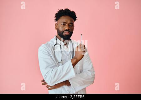 Il chirurgo maschile premuroso tiene la penna mentre guarda la fotocamera su sfondo rosa Foto Stock