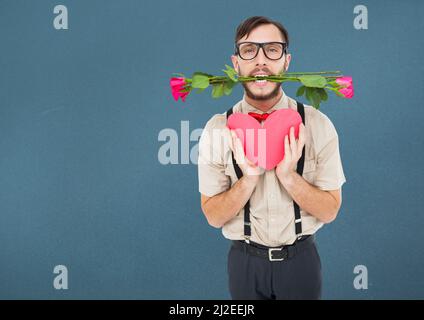 Uomo caucasico con rose in bocca che tiene un cuore rosso contro lo spazio copia su sfondo blu Foto Stock