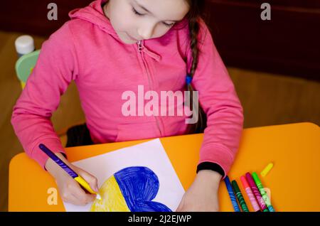 vista ad angolo alto del cuore di disegno della ragazza con bandiera ucraina sul tavolo giallo, immagine di scorta Foto Stock