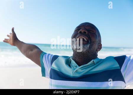 Happy african american senior pensionato uomo con gli occhi chiusi e braccia distese in spiaggia Foto Stock