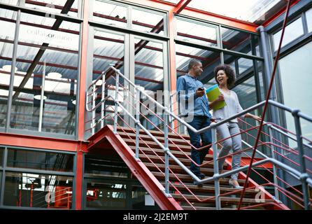 La comunicazione è la chiave del successo. Due colleghi camminano fianco a fianco giù per le scale nel loro edificio. Foto Stock