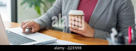 Business analista concetto l'ufficiale femminile che tiene una tazza di caffè digitando informazioni sul computer portatile. Foto Stock